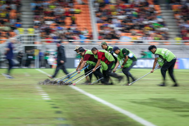 Sejumlah staf Jakarta International Stadium mendorong air keluar dari lapangan, Jumat (24/11/2023) malam WIB. Foto: Bolanet