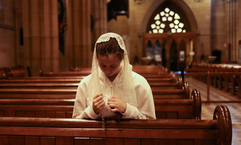 Seorang perempuan muda berdoa rosario di dalam Katedral St Mary di Sydney pada 6 Januari 2021. (Foto CNS/Loren Elliott, Reuters)